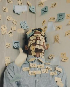 An over extended, stressed business man has a bunch of "to-do" post its stuck to his body. He needs help practicing stress management.